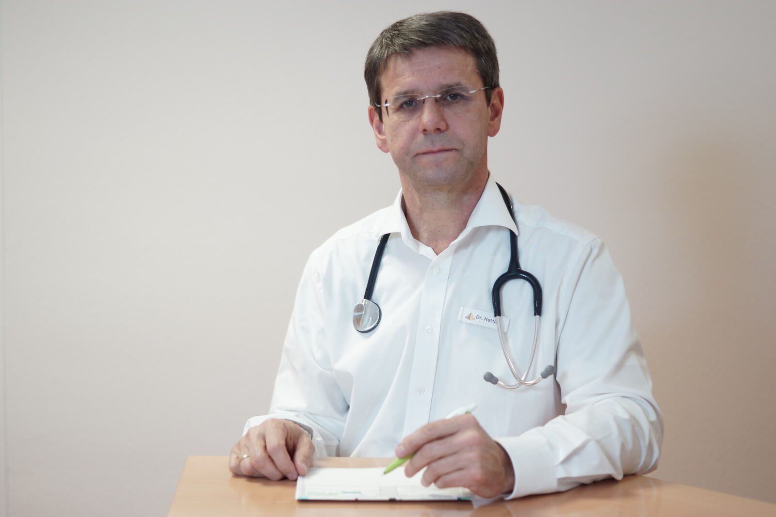 Dr. Armin Hettich am Tisch, freundlich in die Kamera blickend